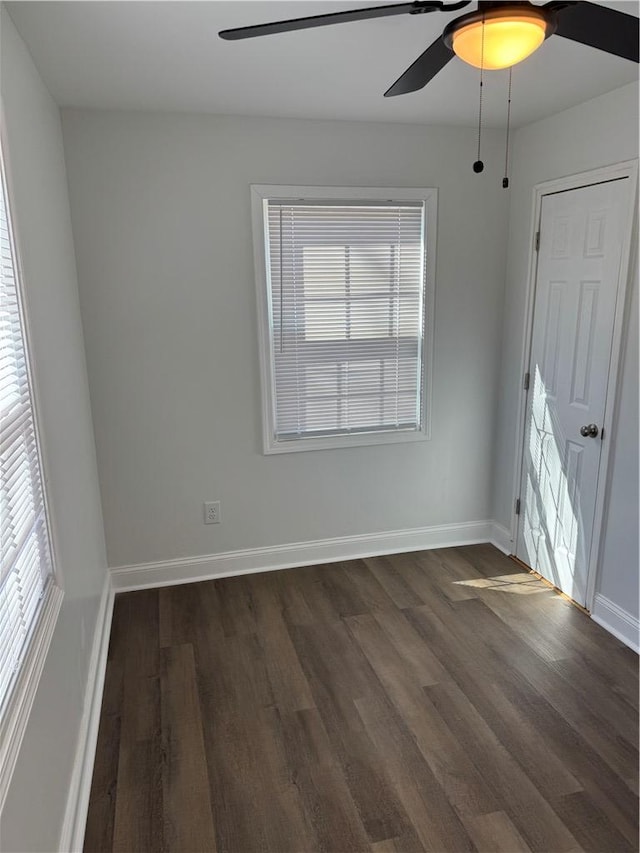 spare room with a wealth of natural light, ceiling fan, baseboards, and dark wood-style flooring