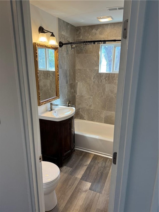 full bathroom with a wealth of natural light, visible vents, toilet, and wood finished floors