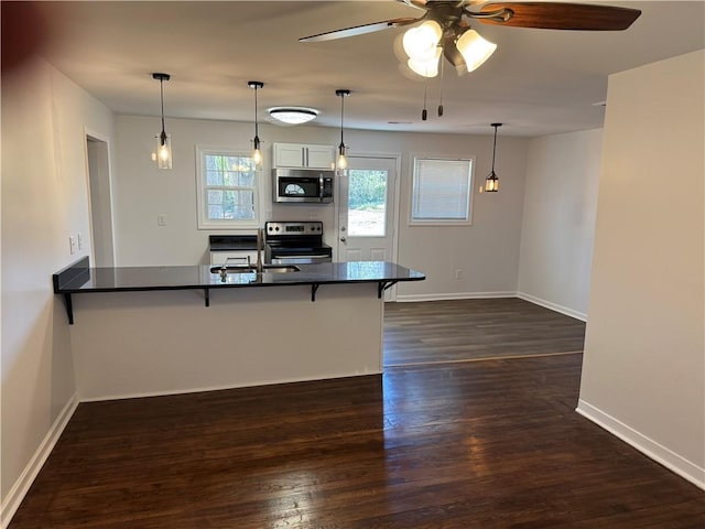 kitchen featuring dark wood finished floors, dark countertops, a peninsula, stainless steel appliances, and a kitchen bar