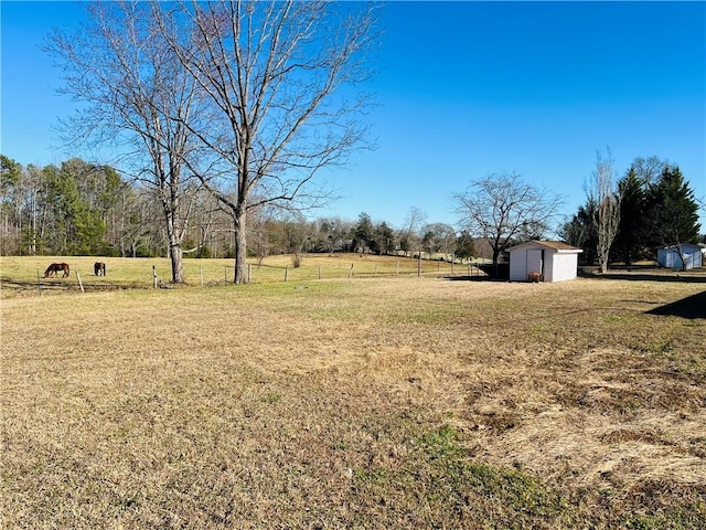 view of yard featuring a storage shed, a rural view, fence, and an outdoor structure