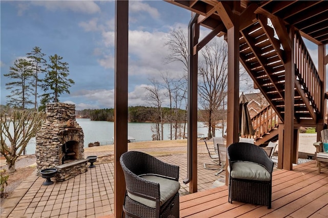 deck with stairs, an outdoor stone fireplace, and a water view