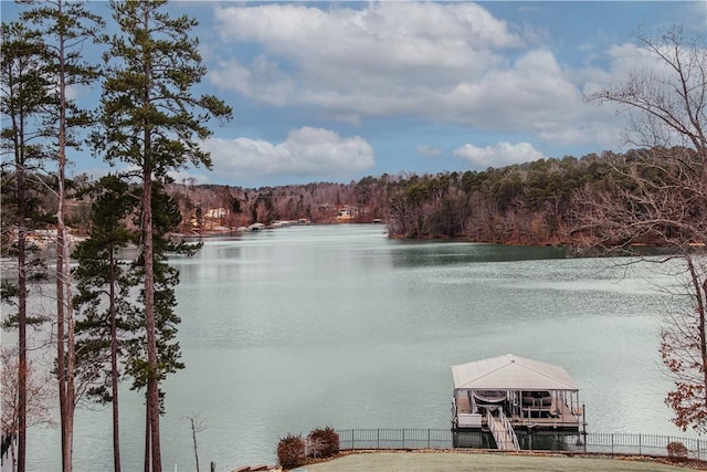 property view of water featuring boat lift, a wooded view, a dock, and fence