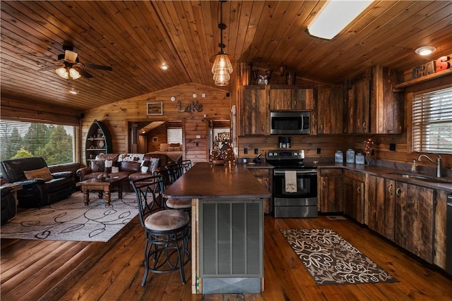 kitchen with stainless steel appliances, dark countertops, open floor plan, a sink, and wooden walls