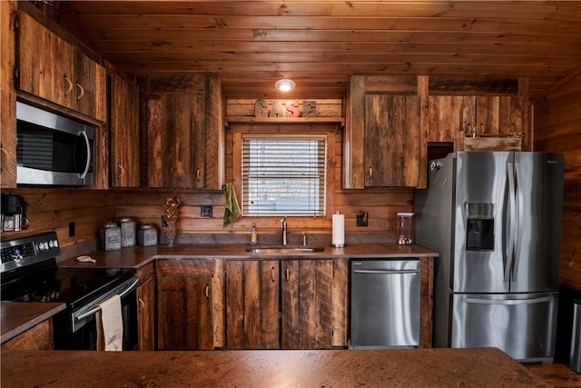 kitchen with dark countertops, appliances with stainless steel finishes, wood ceiling, a sink, and wooden walls