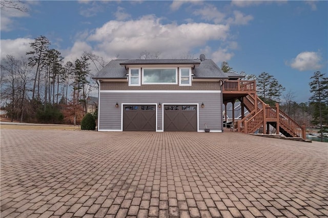 exterior space featuring decorative driveway, an attached garage, a wooden deck, and stairs