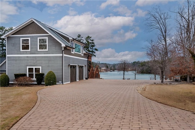 view of property exterior with decorative driveway, a water view, and a lawn