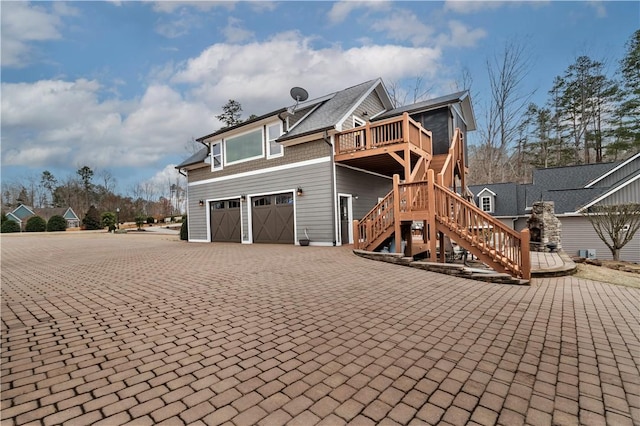 view of property exterior with a garage, decorative driveway, a deck, and stairs