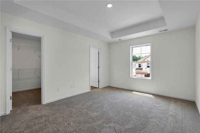 unfurnished bedroom featuring a walk in closet, a raised ceiling, carpet, baseboards, and visible vents