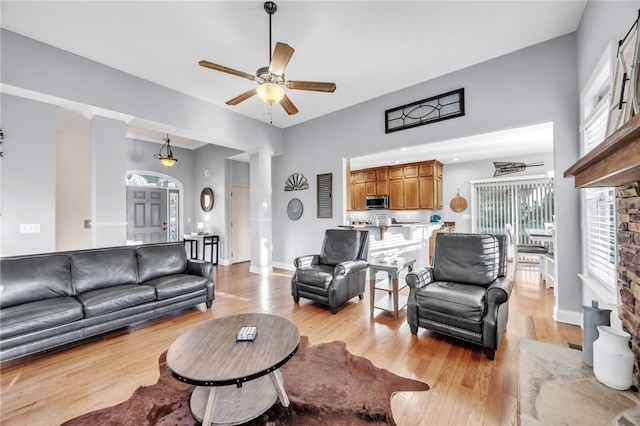 living room featuring a ceiling fan, light wood-type flooring, decorative columns, and baseboards