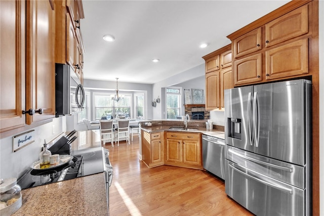 kitchen featuring a peninsula, stainless steel appliances, light wood-type flooring, pendant lighting, and a sink