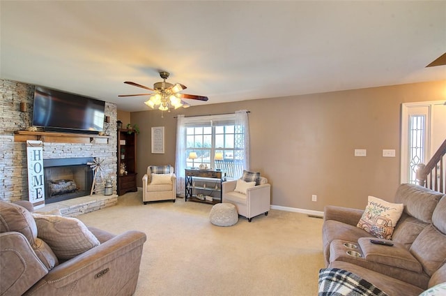 living room with visible vents, light colored carpet, a ceiling fan, a stone fireplace, and baseboards