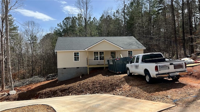 view of front of home with crawl space, a view of trees, and roof with shingles