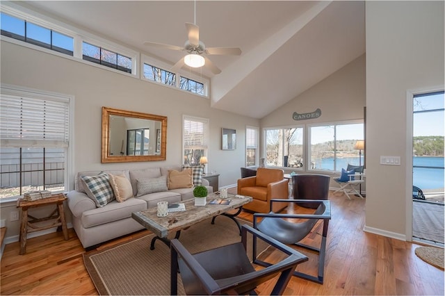 living area with high vaulted ceiling, light wood-type flooring, baseboards, and a ceiling fan