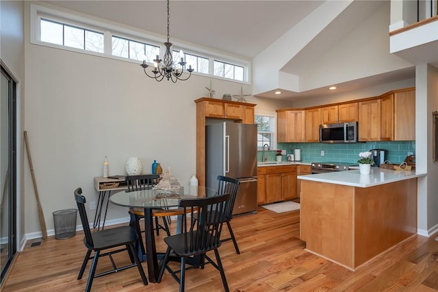 kitchen with a peninsula, light wood-type flooring, tasteful backsplash, and stainless steel appliances