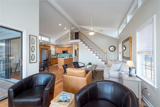 living room featuring plenty of natural light, stairway, light wood-style flooring, and beam ceiling