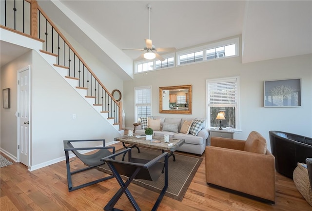 living room with ceiling fan, a towering ceiling, baseboards, stairway, and light wood finished floors