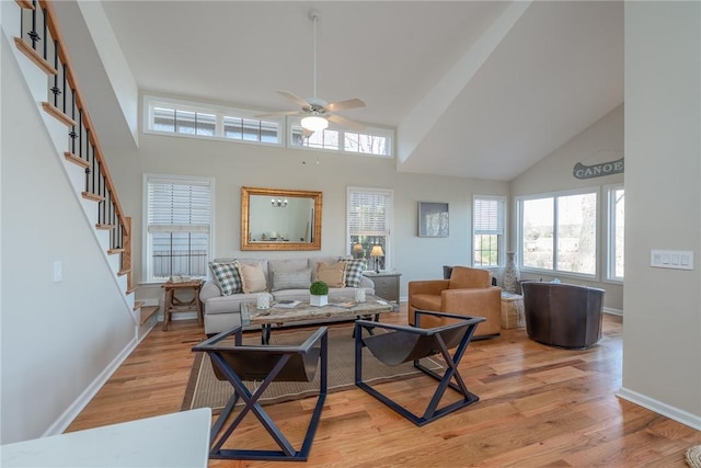 living room with a ceiling fan, light wood-type flooring, baseboards, and stairs