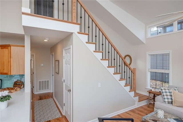 stairway featuring baseboards, visible vents, a high ceiling, and wood finished floors