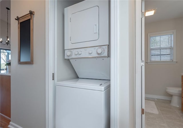 laundry room featuring laundry area, baseboards, stacked washer and clothes dryer, a notable chandelier, and light tile patterned flooring