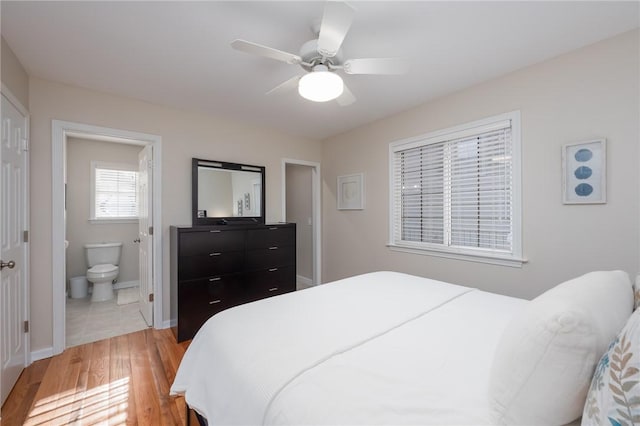 bedroom with baseboards, ceiling fan, ensuite bath, and light wood finished floors