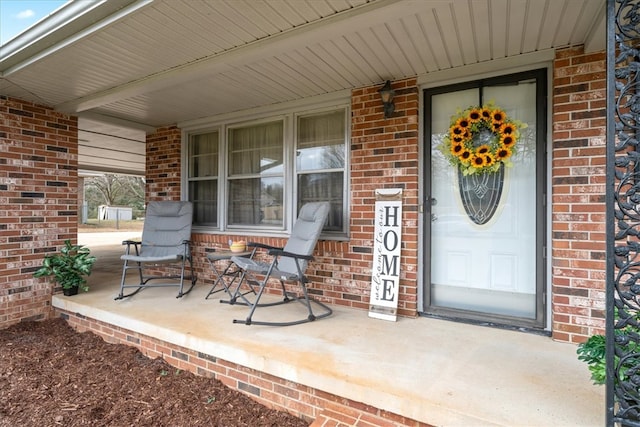 doorway to property featuring covered porch and brick siding