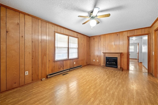 unfurnished living room featuring light wood finished floors, baseboard heating, a textured ceiling, and a glass covered fireplace