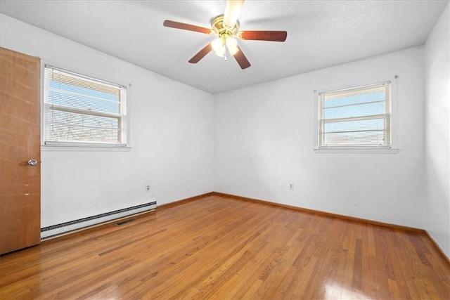 spare room featuring a ceiling fan, baseboard heating, light wood-style flooring, and baseboards