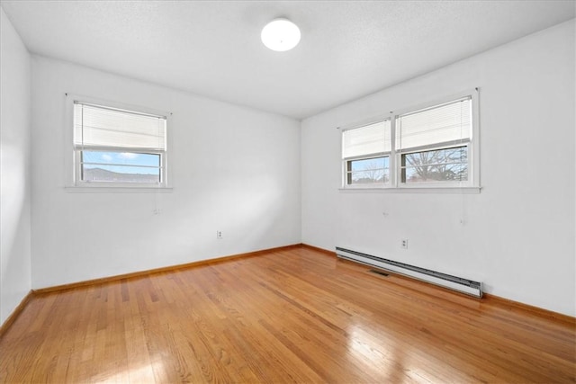 spare room with a baseboard radiator, light wood-style flooring, and baseboards