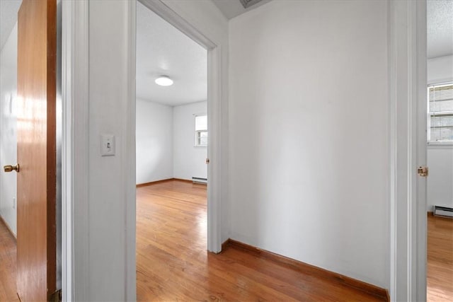 hall featuring light wood-style flooring, baseboards, baseboard heating, and a textured ceiling