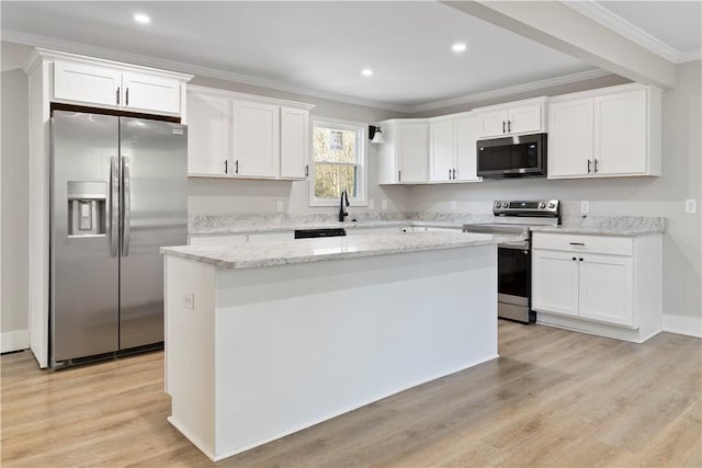 kitchen with light wood finished floors, white cabinets, a kitchen island, ornamental molding, and stainless steel appliances