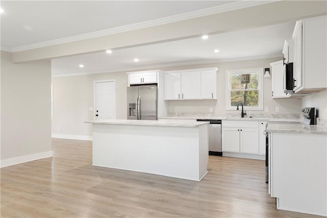 kitchen featuring appliances with stainless steel finishes, light wood-style floors, ornamental molding, a kitchen island, and a sink