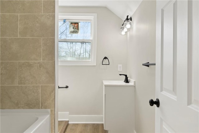 bathroom with lofted ceiling, a bathing tub, wood finished floors, vanity, and baseboards