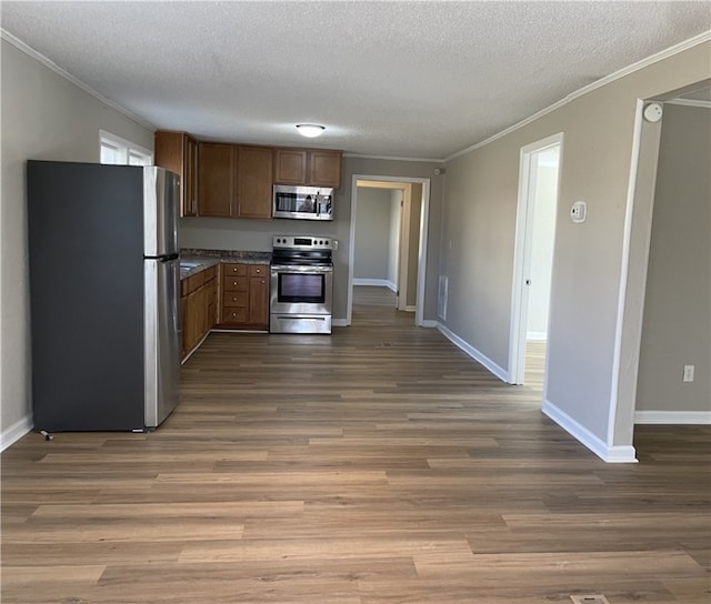 kitchen with a textured ceiling, ornamental molding, stainless steel appliances, and wood finished floors