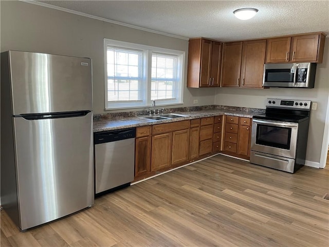 kitchen with stainless steel appliances, a sink, light wood-style floors, dark countertops, and crown molding