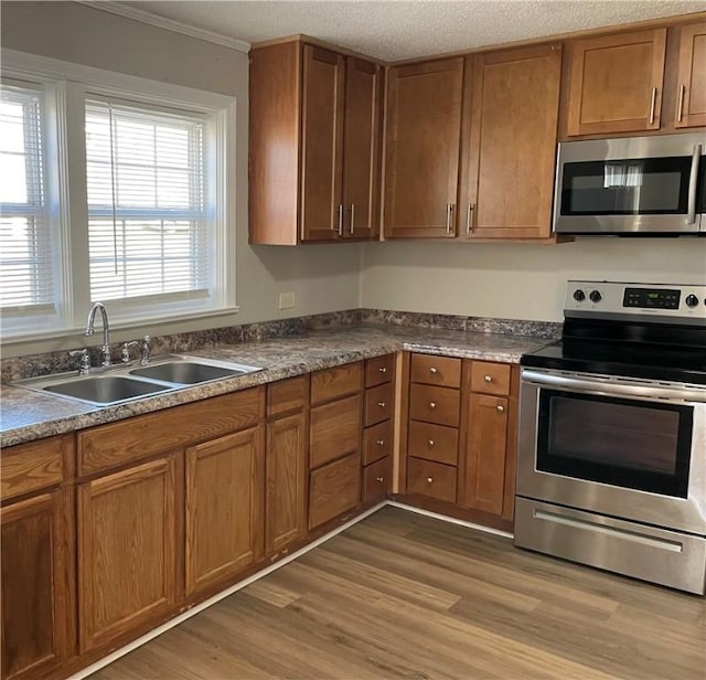 kitchen with a textured ceiling, light wood-style flooring, a sink, appliances with stainless steel finishes, and brown cabinetry