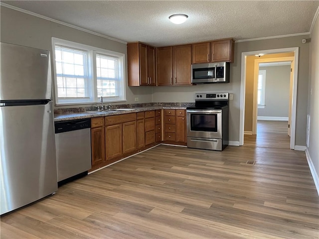 kitchen with appliances with stainless steel finishes, a sink, light wood-style flooring, and crown molding