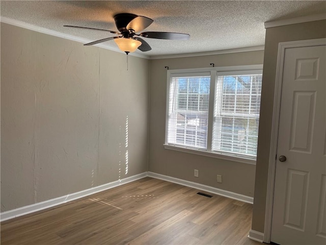 empty room featuring crown molding, visible vents, a textured ceiling, wood finished floors, and baseboards