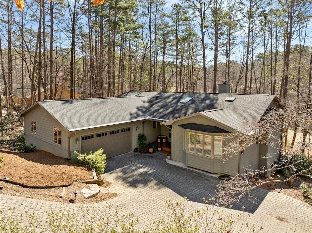 ranch-style house featuring an attached garage, a shingled roof, a chimney, and decorative driveway