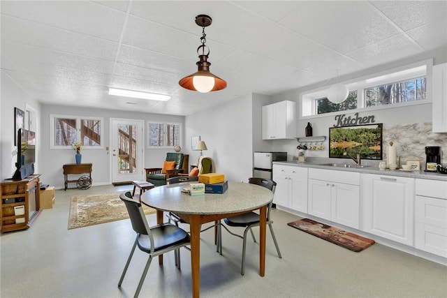 dining area featuring finished concrete flooring, a paneled ceiling, and baseboards