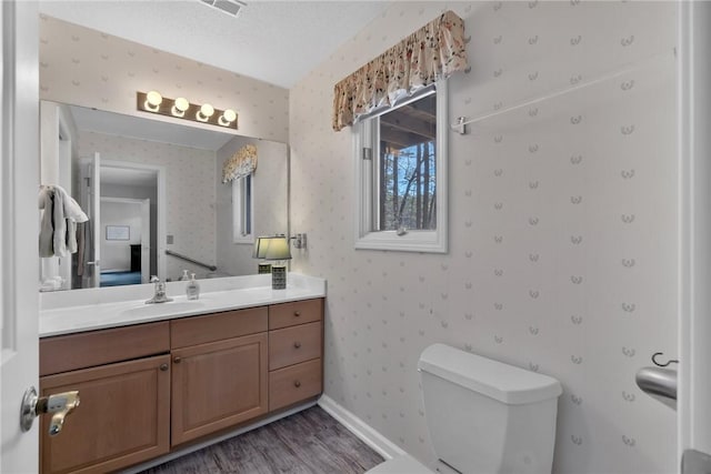 bathroom featuring toilet, wallpapered walls, baseboards, and wood finished floors