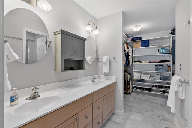 bathroom with marble finish floor, a sink, a spacious closet, and double vanity