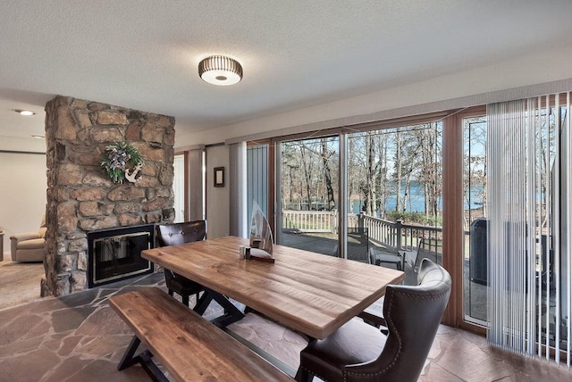 dining room featuring plenty of natural light, stone finish floor, a textured ceiling, and a stone fireplace