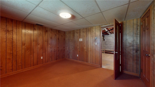 spare room featuring wooden walls, baseboards, a drop ceiling, and carpet flooring