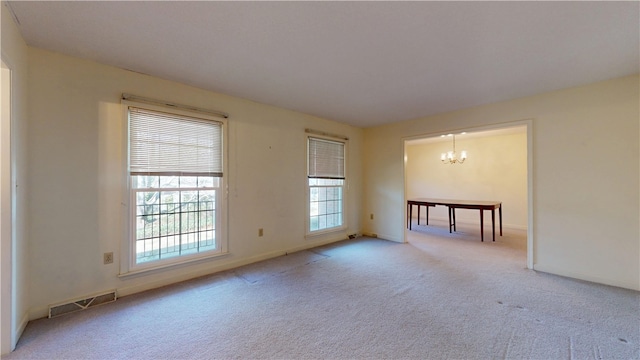 empty room with a chandelier, carpet floors, visible vents, and baseboards