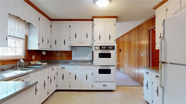 kitchen featuring white cabinets, wood walls, a sink, white appliances, and under cabinet range hood