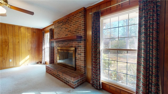 unfurnished living room with a healthy amount of sunlight, a brick fireplace, wooden walls, and carpet flooring