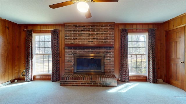 unfurnished living room with carpet floors, plenty of natural light, a fireplace, and wooden walls