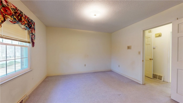 empty room with light carpet, baseboards, visible vents, and a textured ceiling