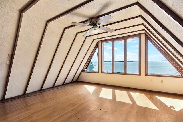 bonus room featuring light wood finished floors, lofted ceiling, ceiling fan, a water view, and a textured ceiling