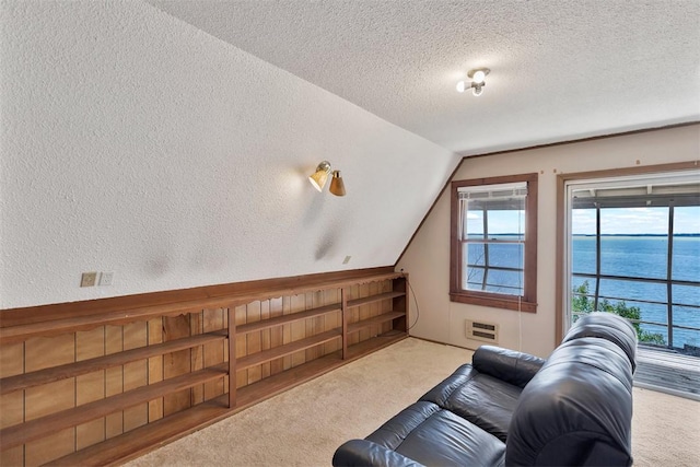 carpeted living area featuring a water view, vaulted ceiling, a textured ceiling, and a textured wall